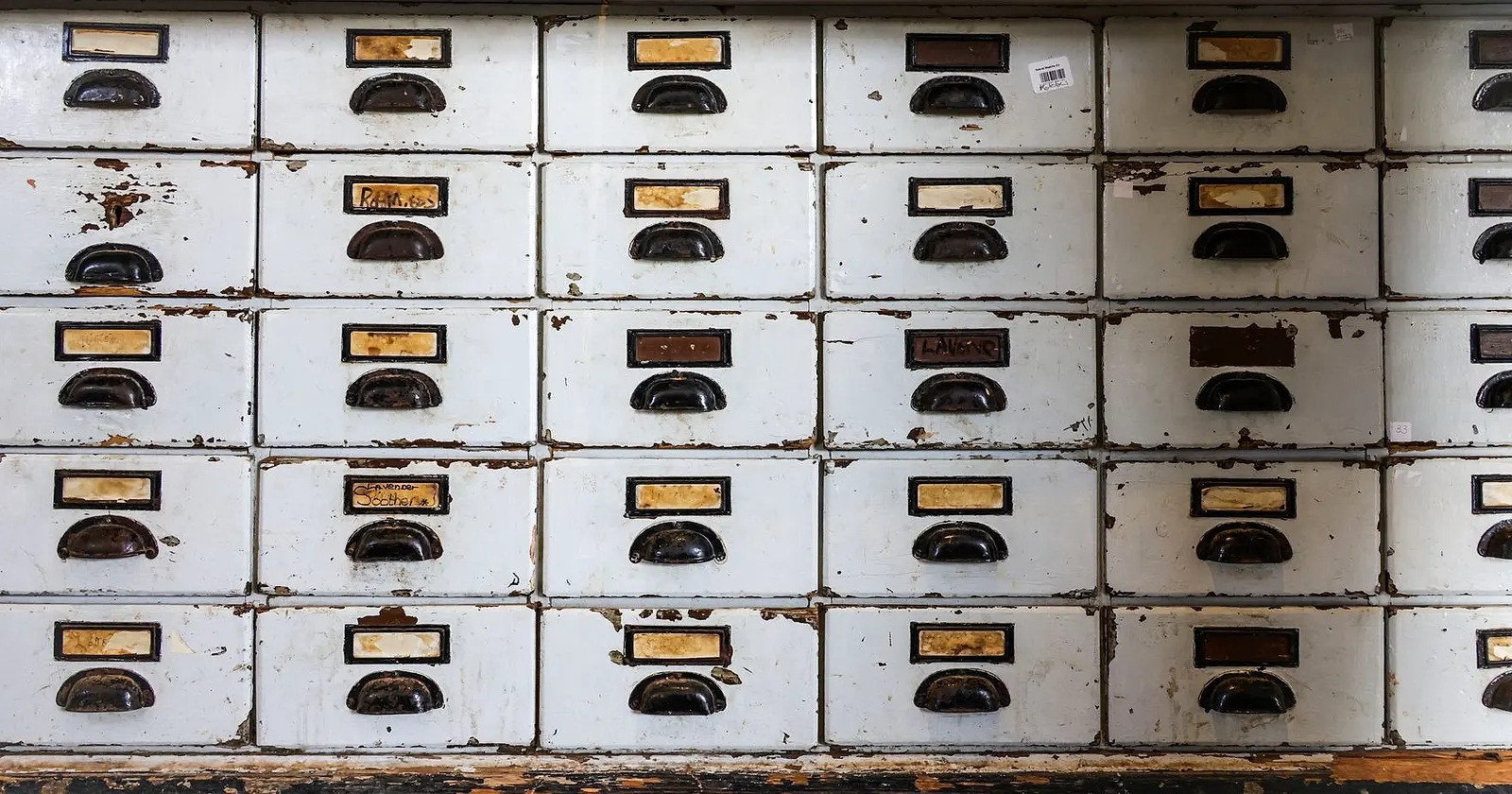 Rows of worn white archive drawers with small brass label holders and dark handles